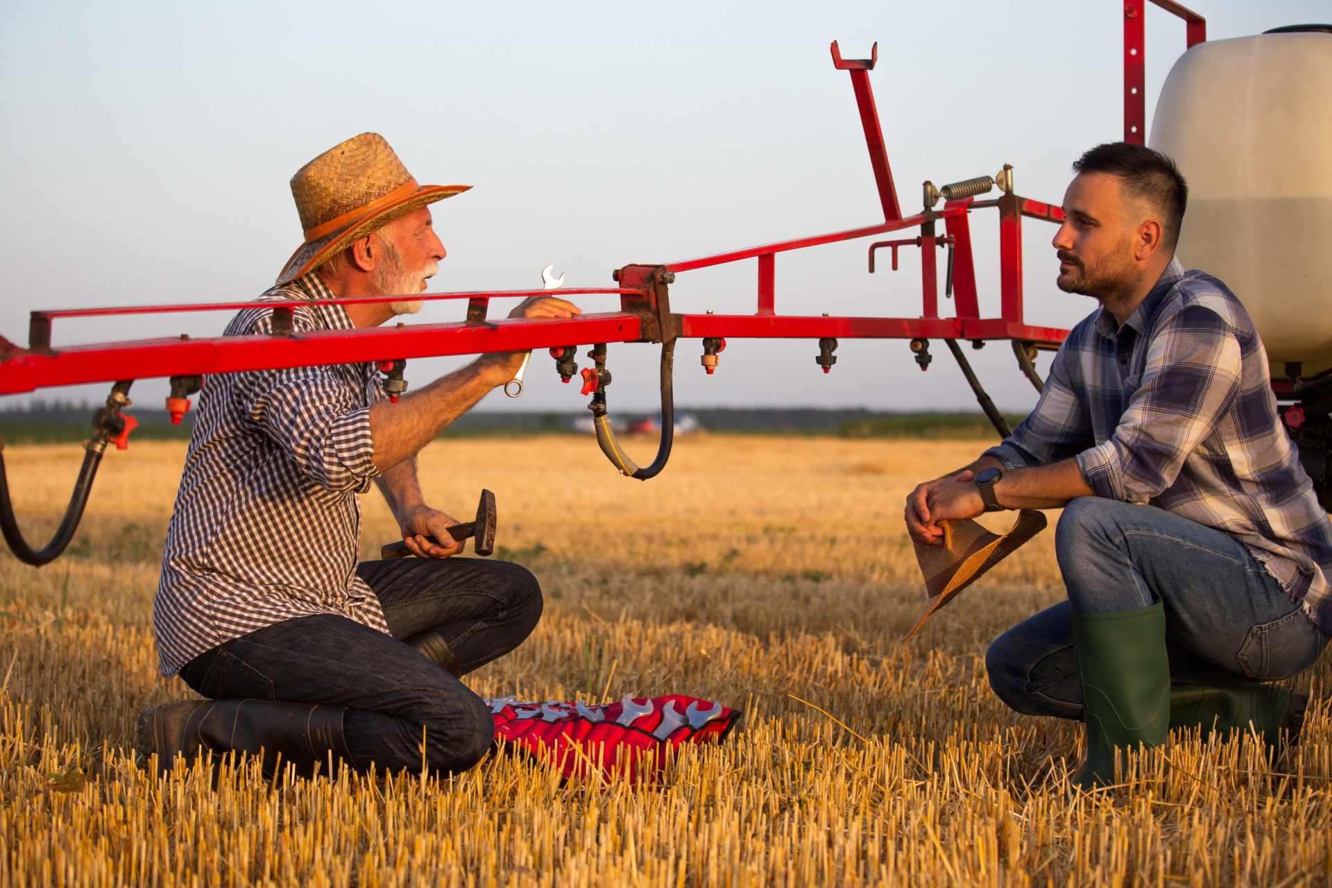 A farmer holding wrench and hammer repairing glyphosate boom sprayer on a tractor.