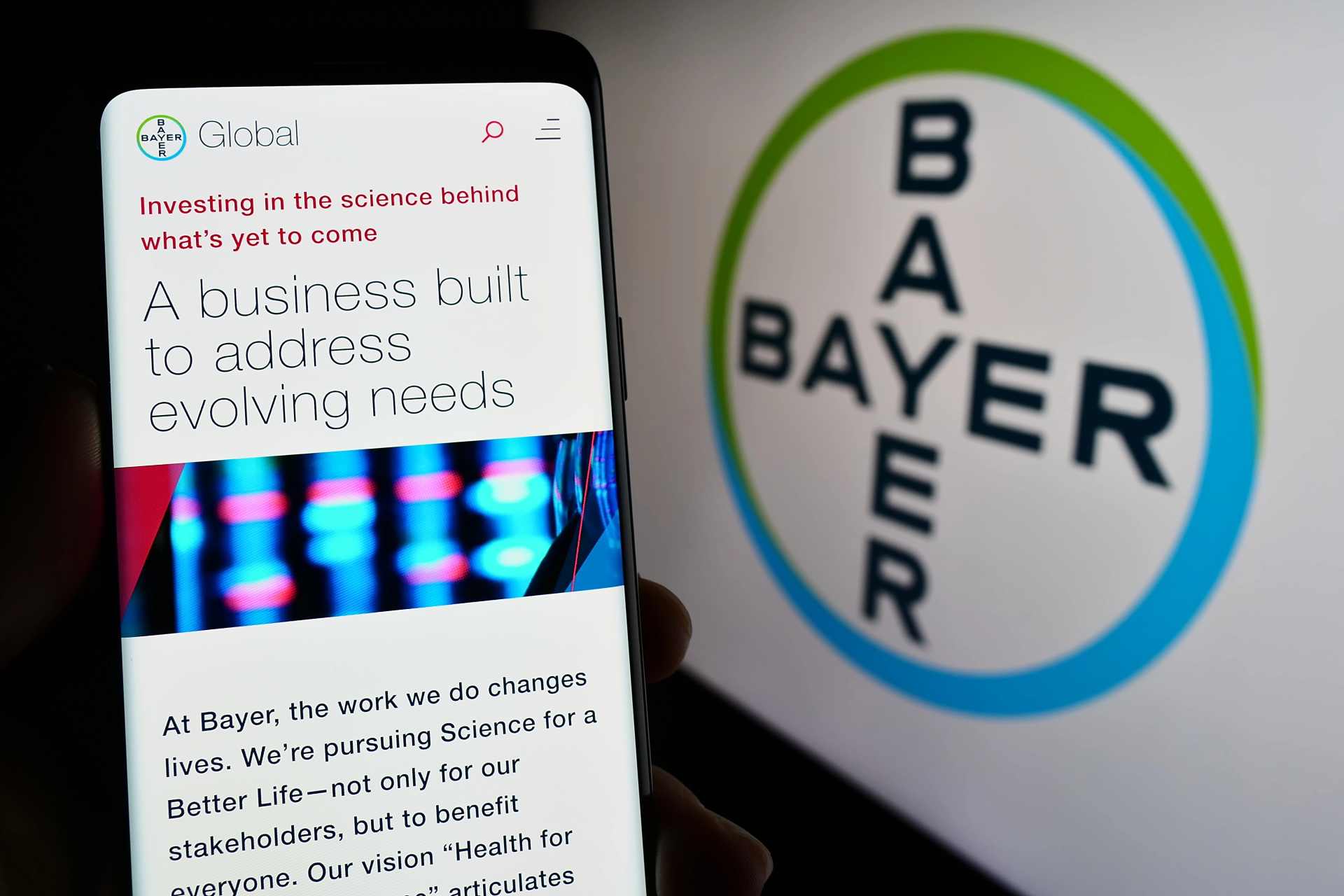 Person holding a smartphone displaying Bayer AG’s website, with the Bayer company logo visible in the background.