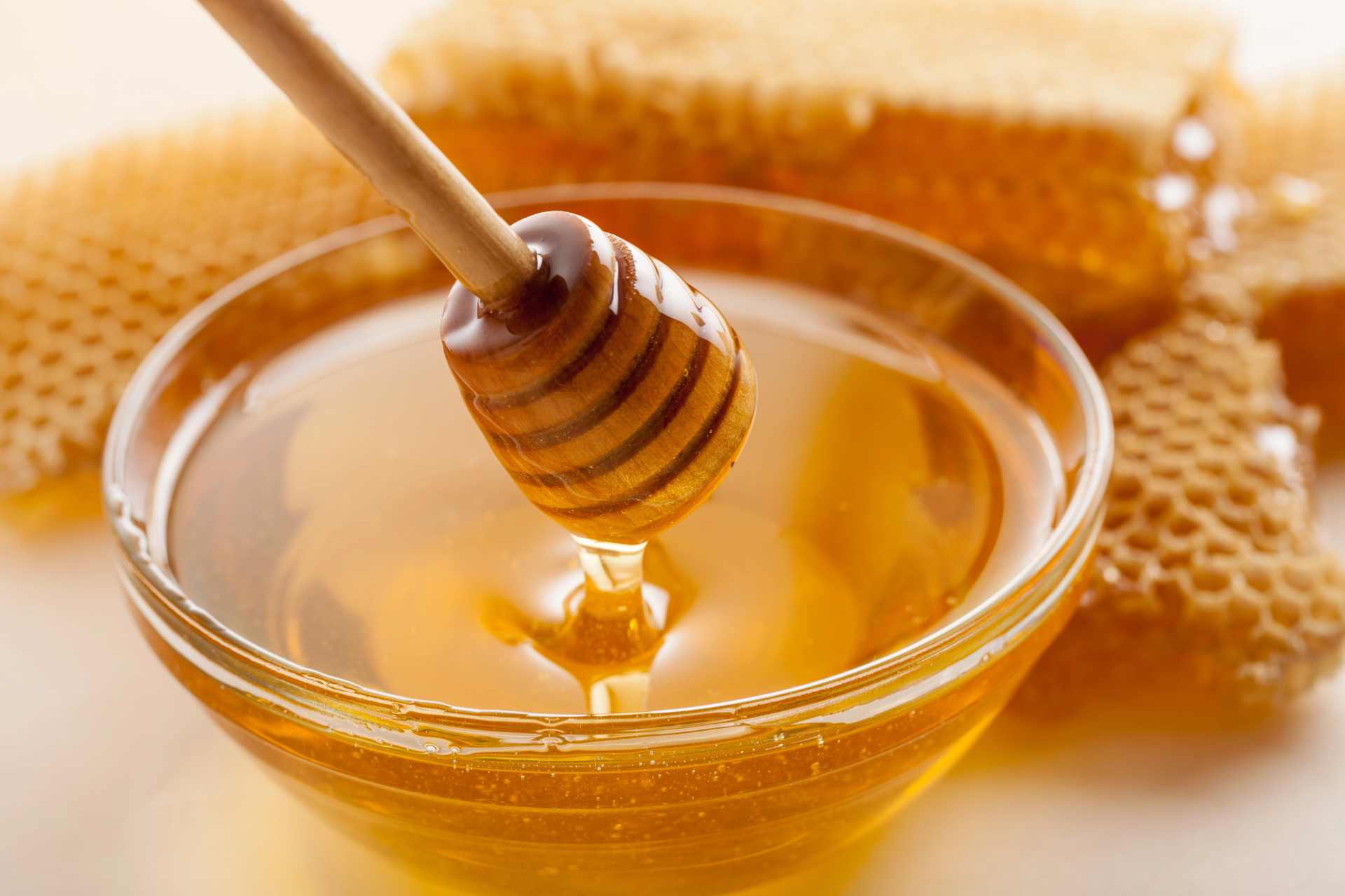 A honey spoon drizzling golden honey with honeycomb in the background, symbolising New Zealand honey tested for glyphosate residues