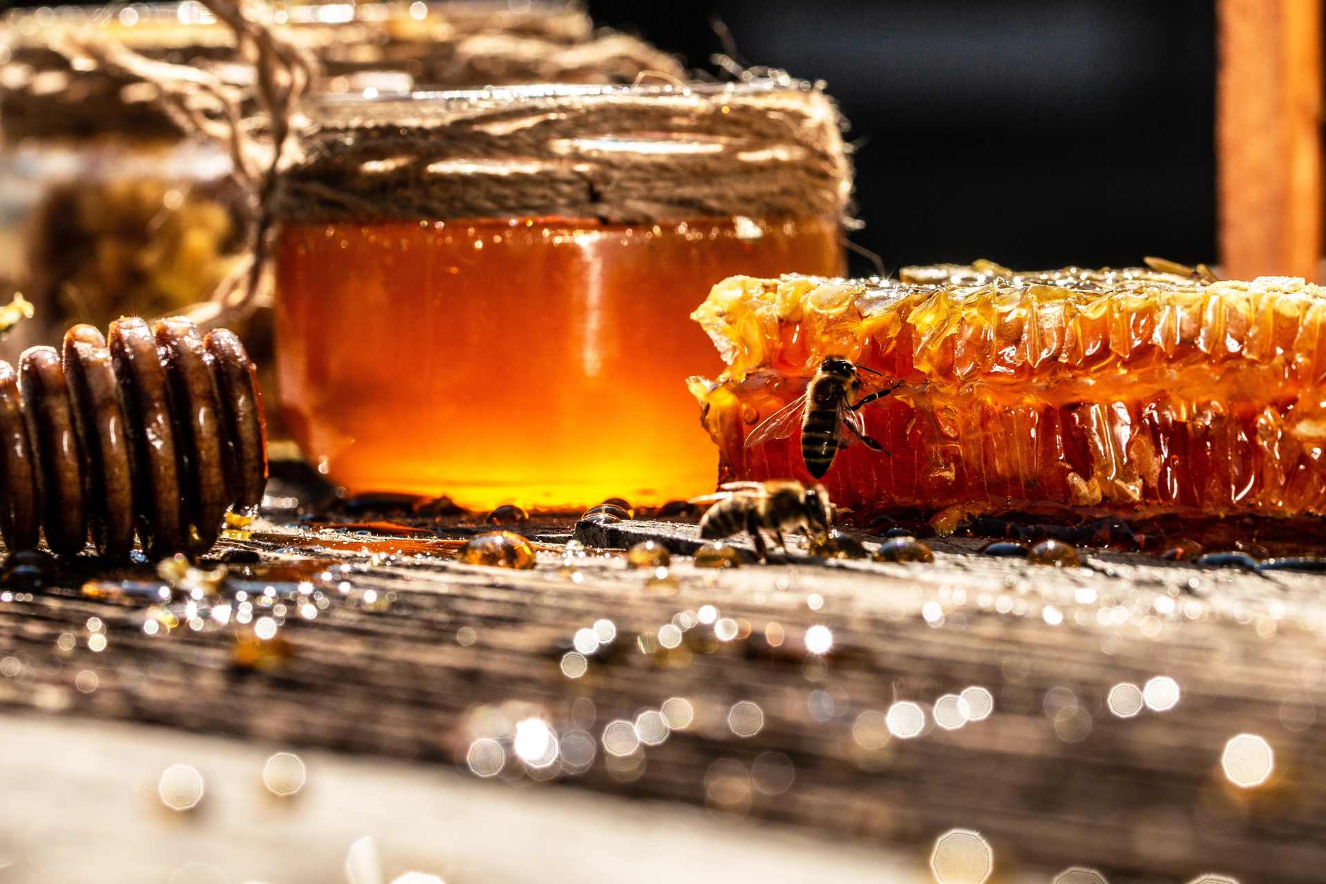 A close-up of a honeycomb and glass jar of honey on a rustic wooden table, symbolizing natural purity and the connection between bees, honey, and environmental health.