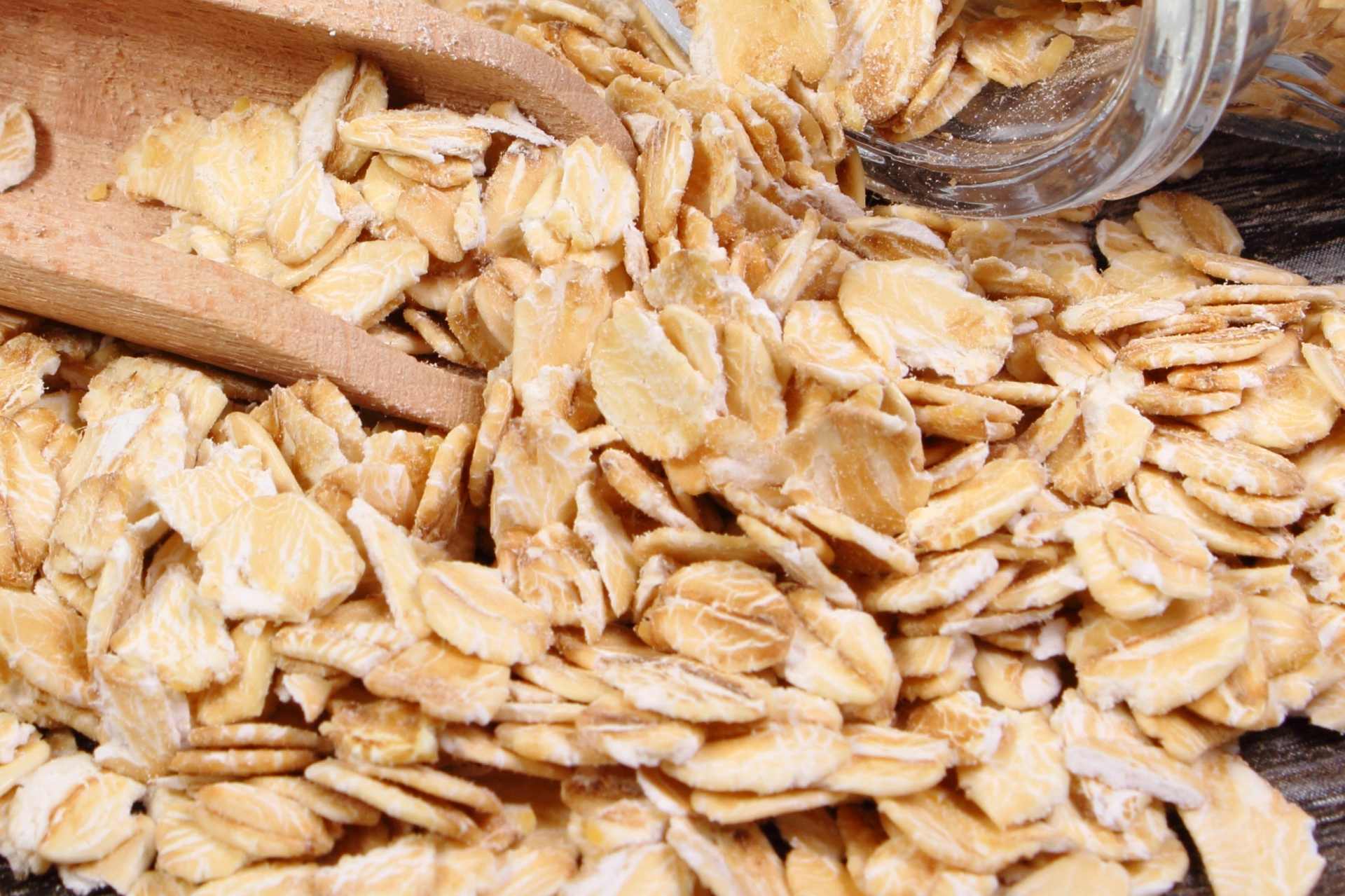 Glass jar tipped on its side with oat flakes spilling out onto a wooden surface, representing everyday oat products being tested for glyphosate residues.