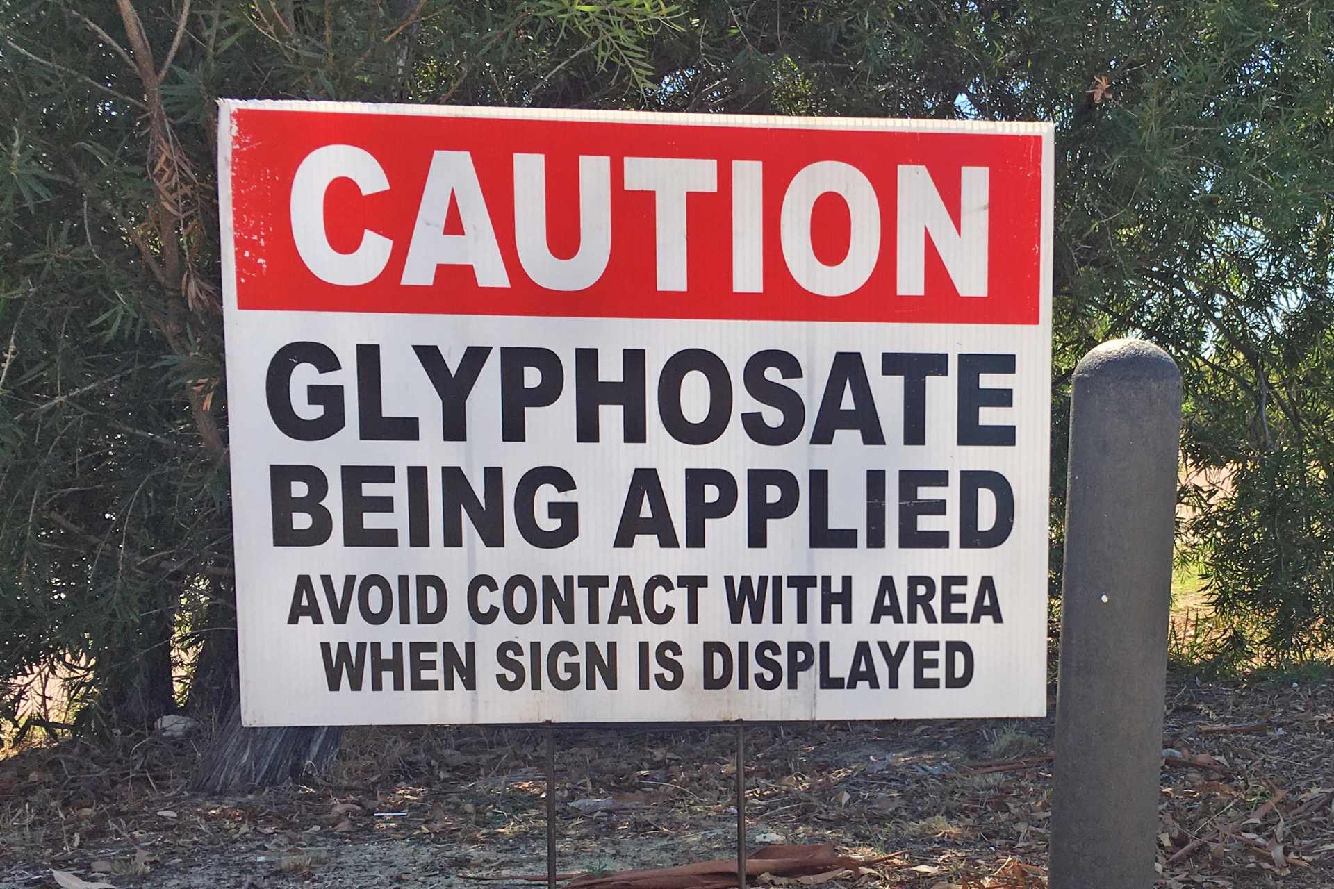 Warning sign stating “Caution: Glyphosate being applied. Avoid contact with area when sign is displayed,” highlighting potential exposure risks from herbicide spraying.
