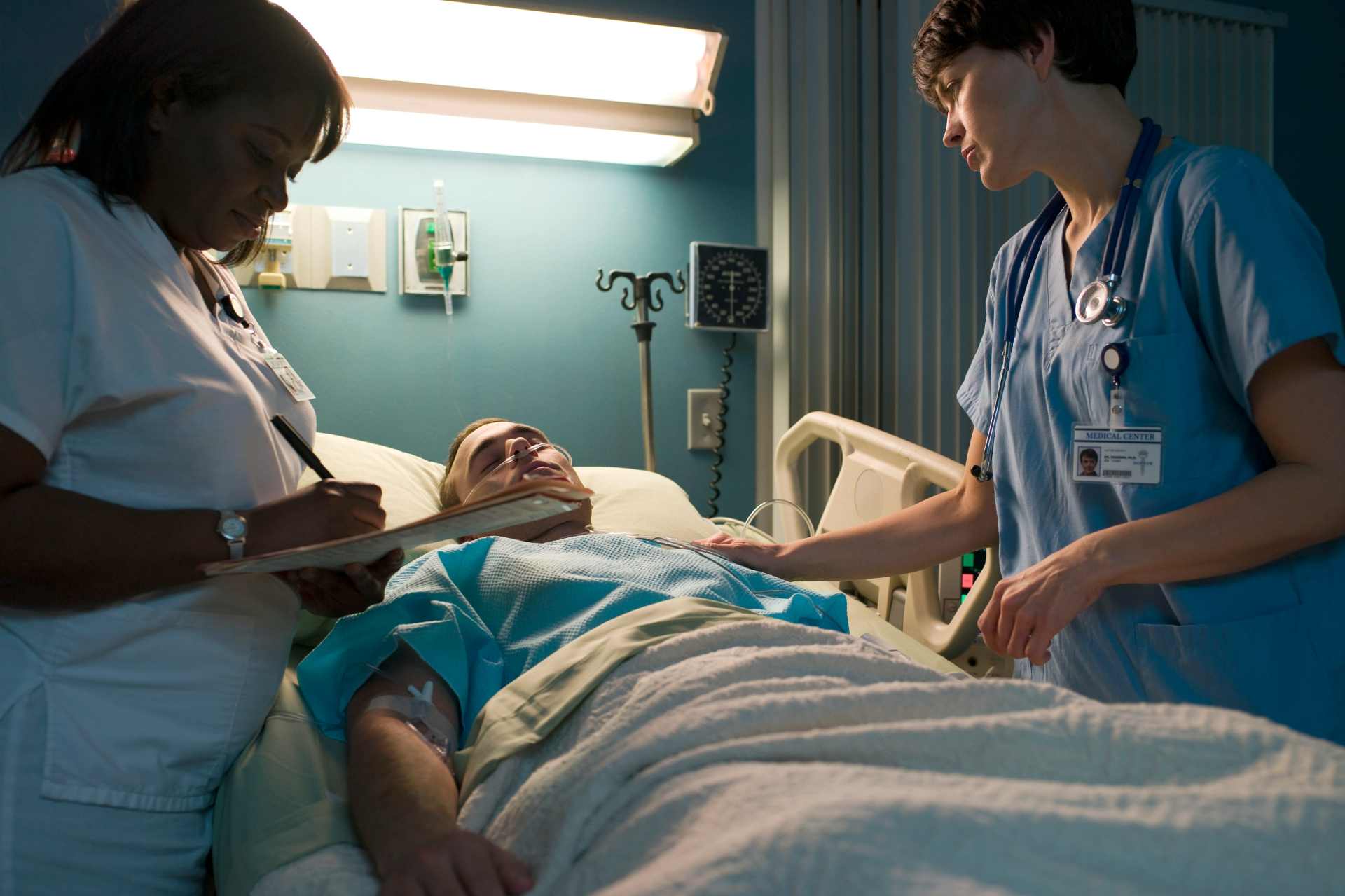 Male patient lying in a hospital bed with two nurses standing beside him, symbolising the human cost of everyday chemical exposure and the reality of living with glyphosate-linked illness.
