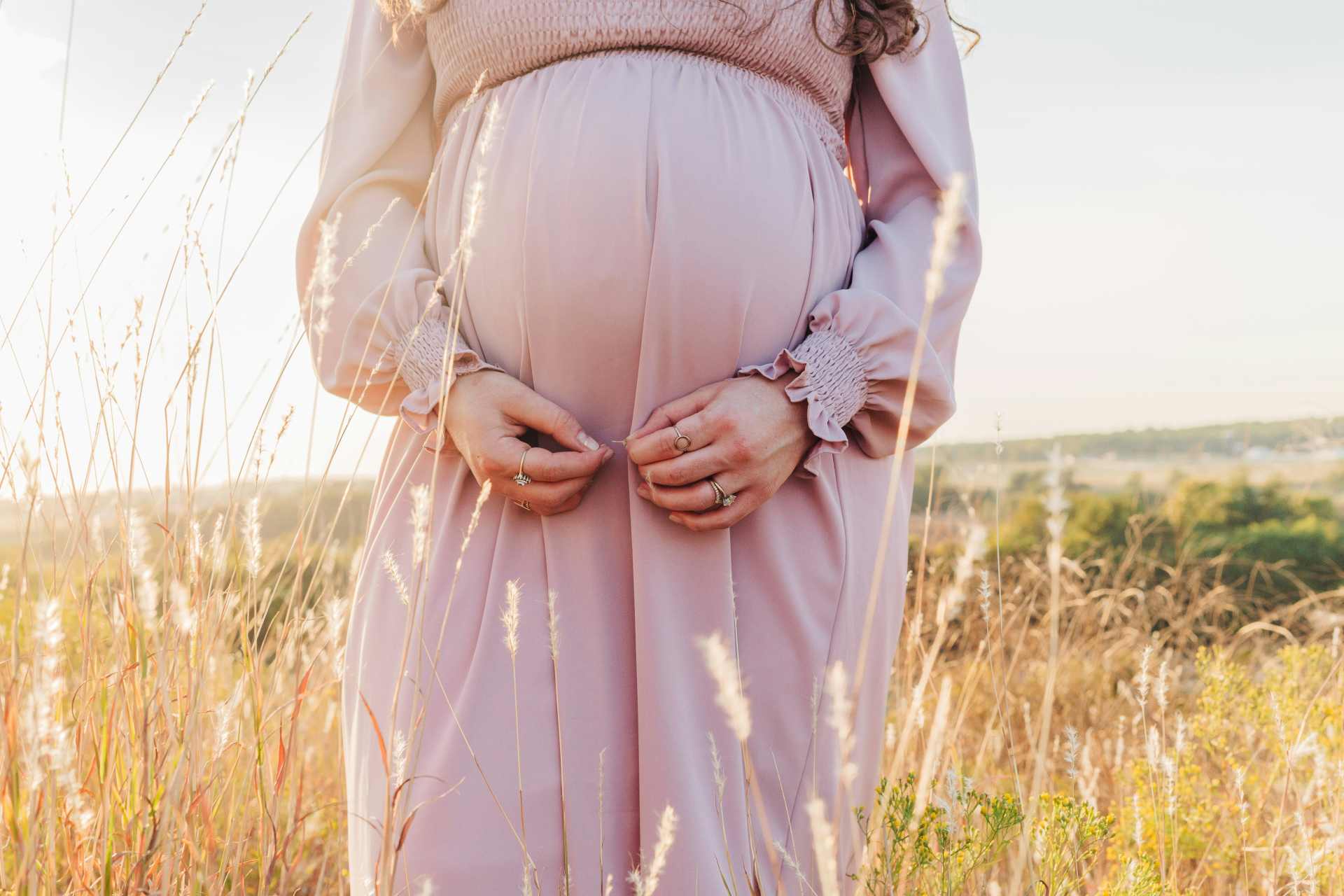Close-up of a pregnant woman standing in long, dry grass, symbolizing vulnerability to hidden environmental exposures during pregnancy.