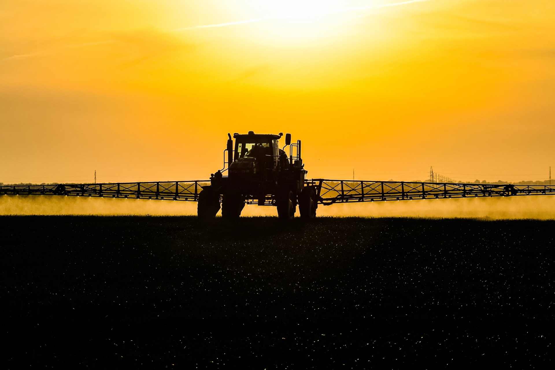 A tractor spraying glyphosate from long boom arms at dusk, illustrating widespread agricultural herbicide application