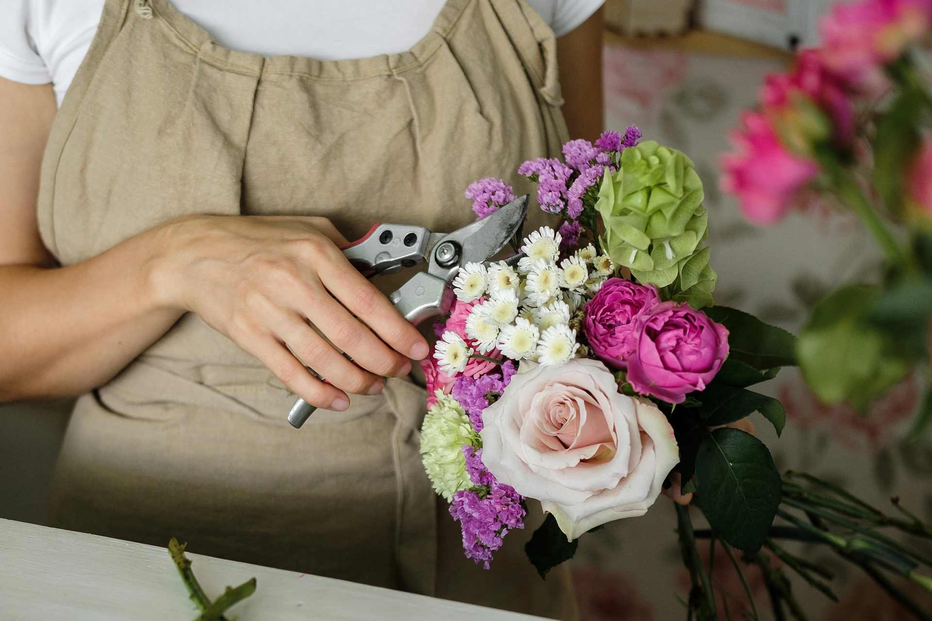 Woman florist arranging a bouquet of pink flowers in a workshop setting.