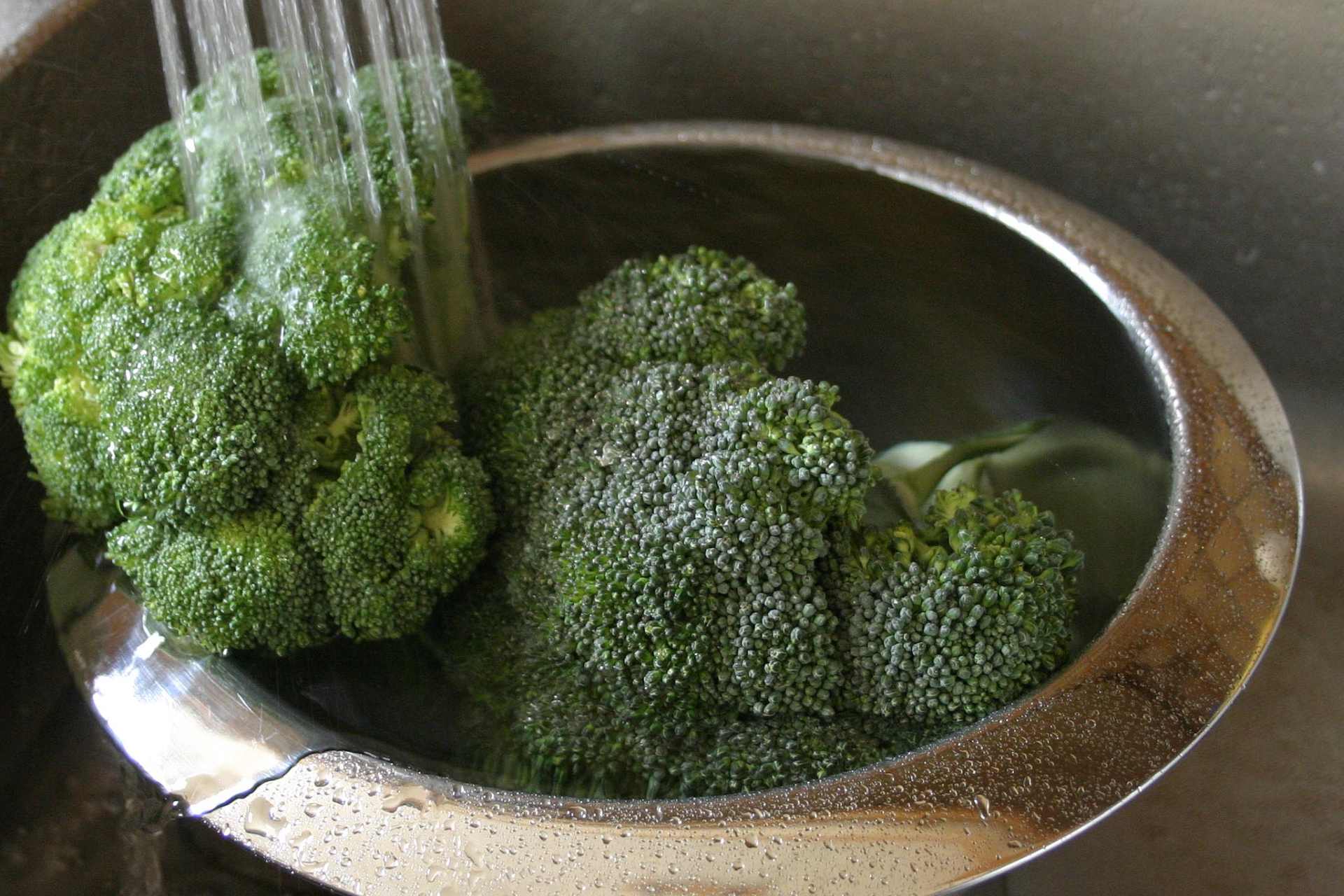 Fresh broccoli being washed under running water in a kitchen sink.