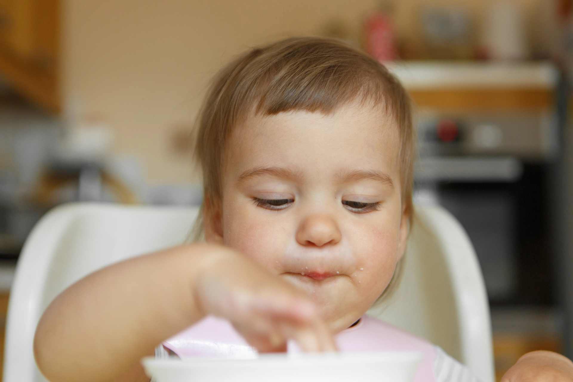 Infant eating cereal with hands during early self-feeding stage.