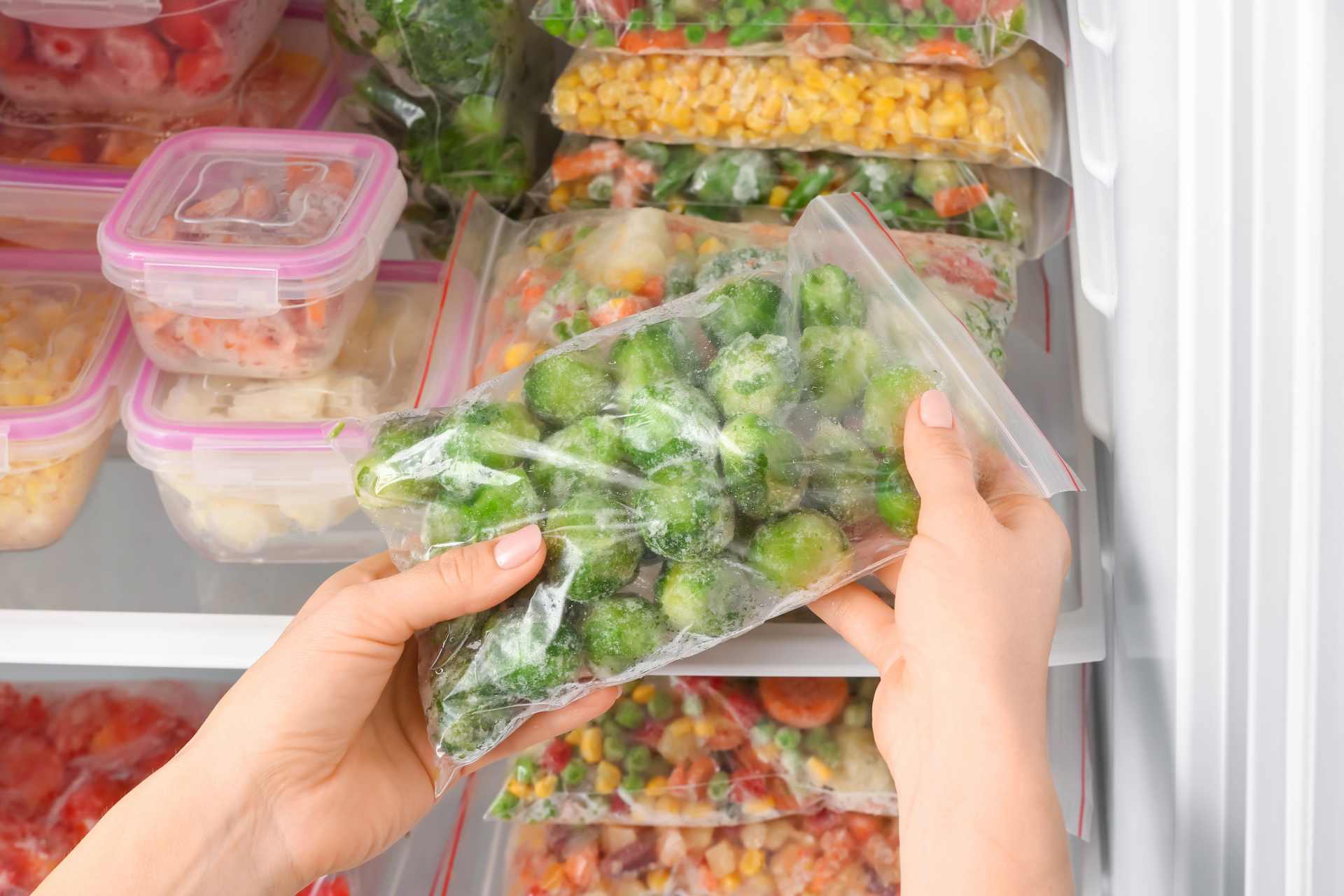 Woman placing a bag of frozen vegetables into a refrigerator freezer, illustrating everyday food storage and freezing practices.