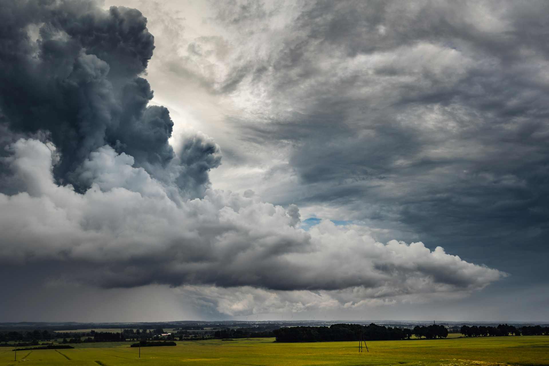 Dark storm clouds forming over rural farmland, with fields stretching beneath a heavy sky