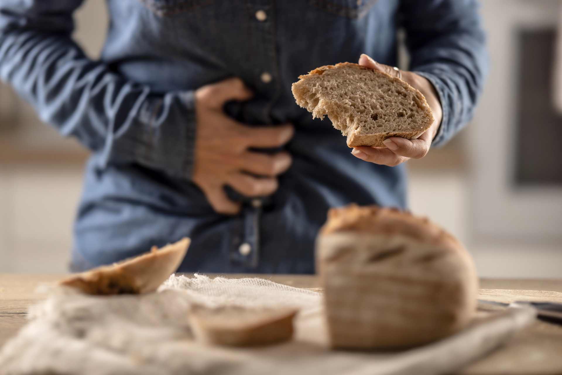 Person holding stomach in discomfort while holding bread — illustrating the question of whether glyphosate residues on wheat, not gluten itself, may be driving the rise in celiac disease and gluten sensitivity in New Zealand