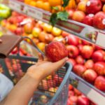 Young woman choosing a fresh red apple while shopping in the fruit and vegetable section of a supermarket.