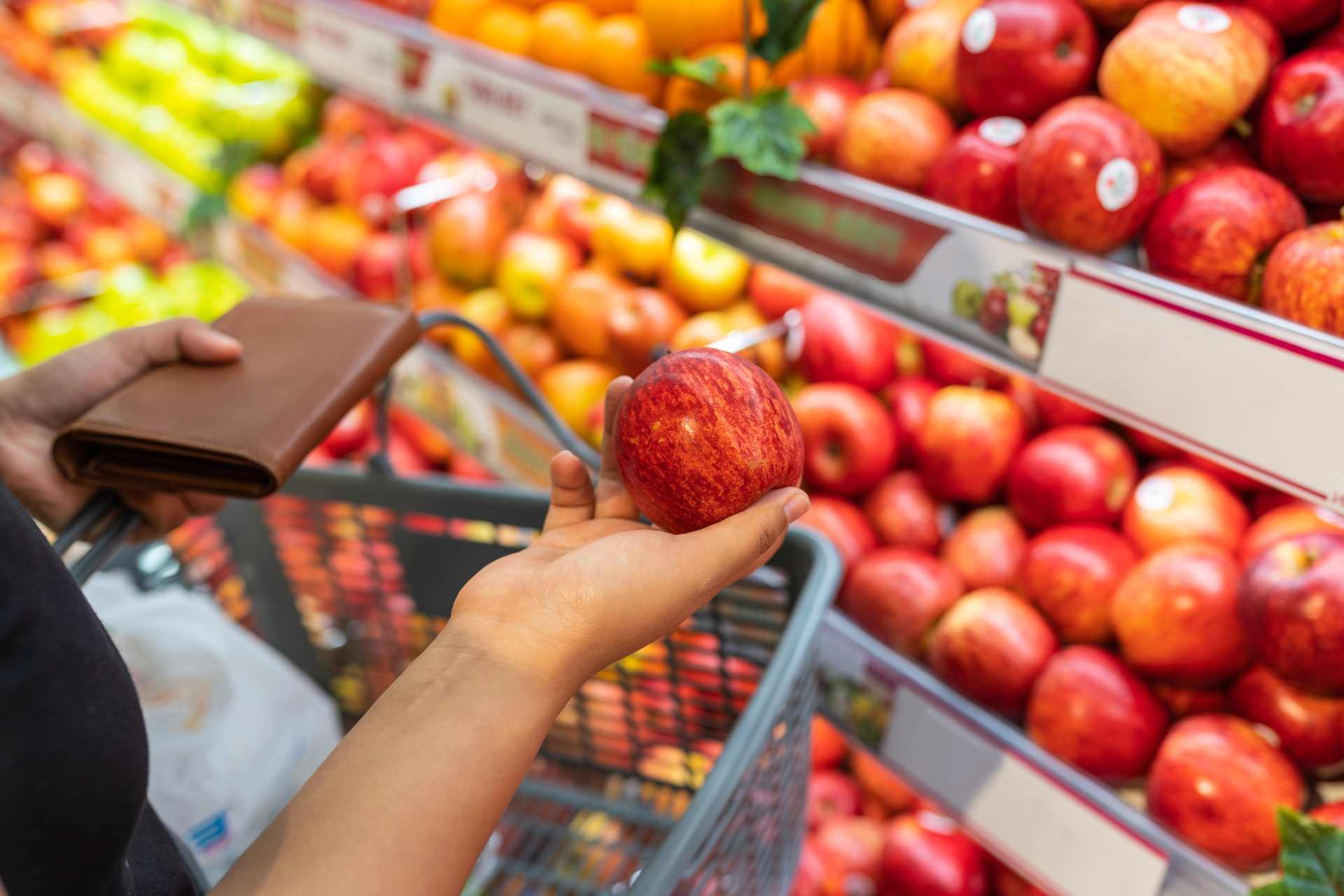 Young woman choosing a fresh red apple while shopping in the fruit and vegetable section of a supermarket.