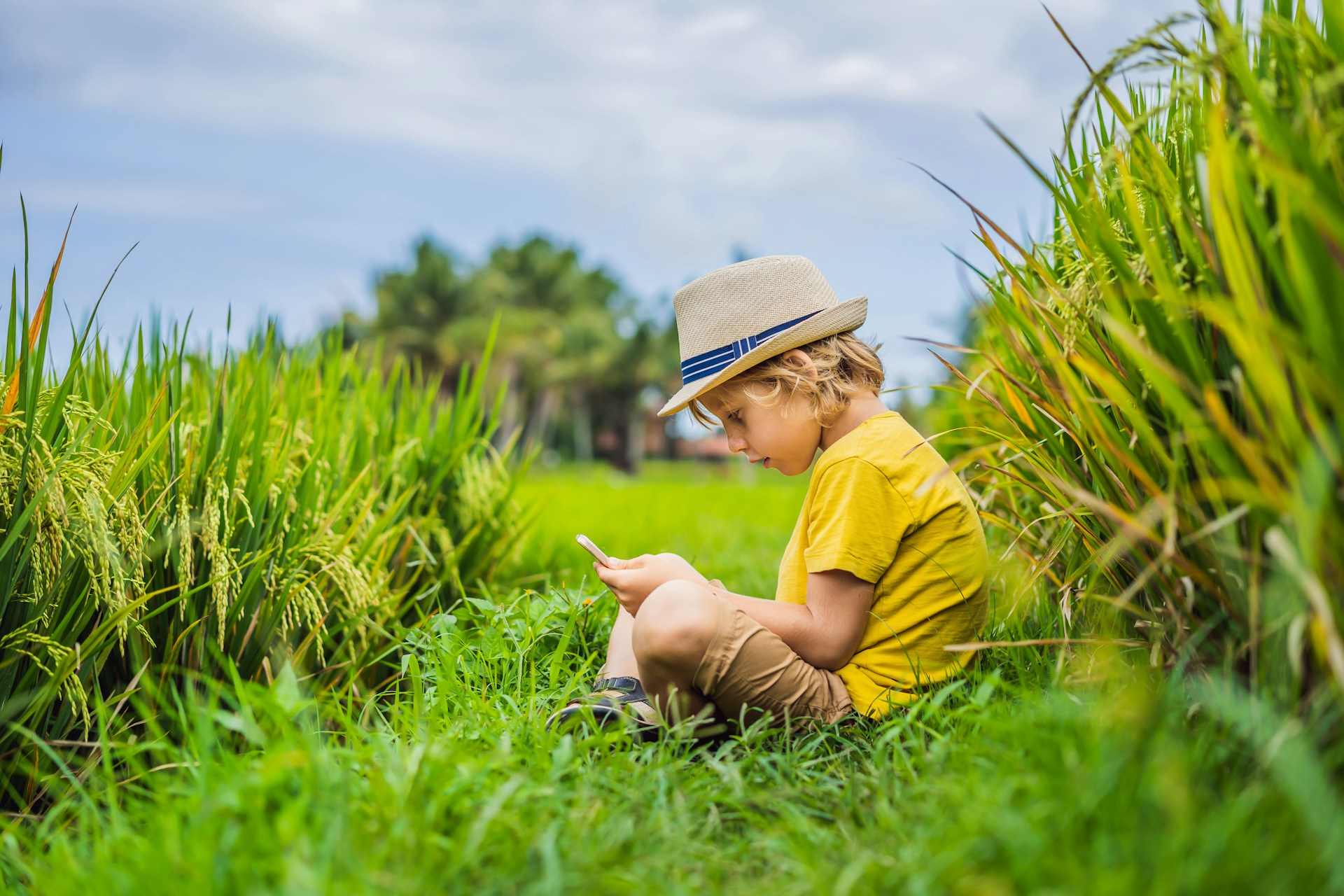 Young boy sitting in grass beside a crop field, representing questions about early-life glyphosate exposure and possible long-term effects.