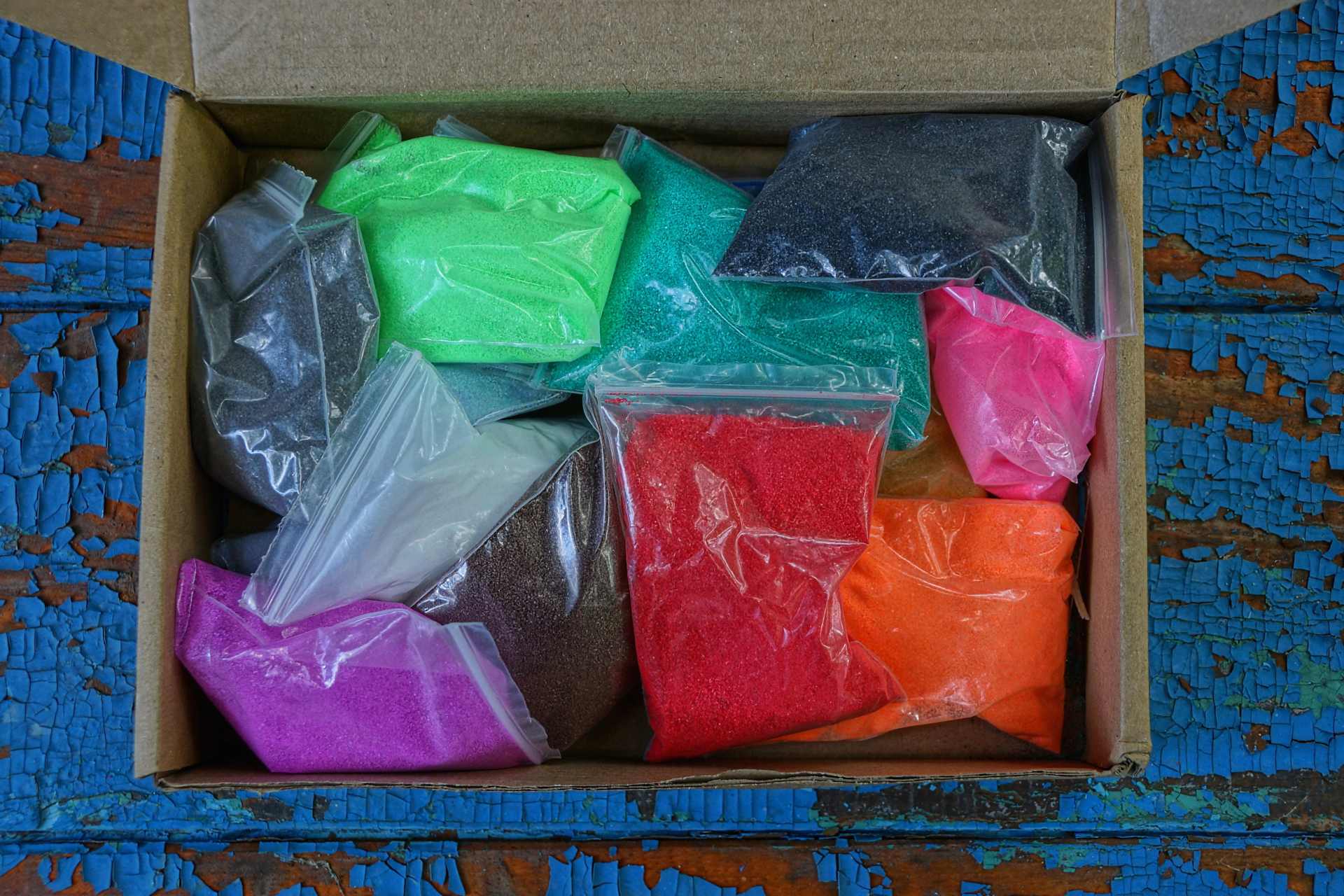 Plastic bags of brightly coloured children’s sand in an open cardboard box, illustrating New Zealand’s proposed precautionary safety measures for sand products.